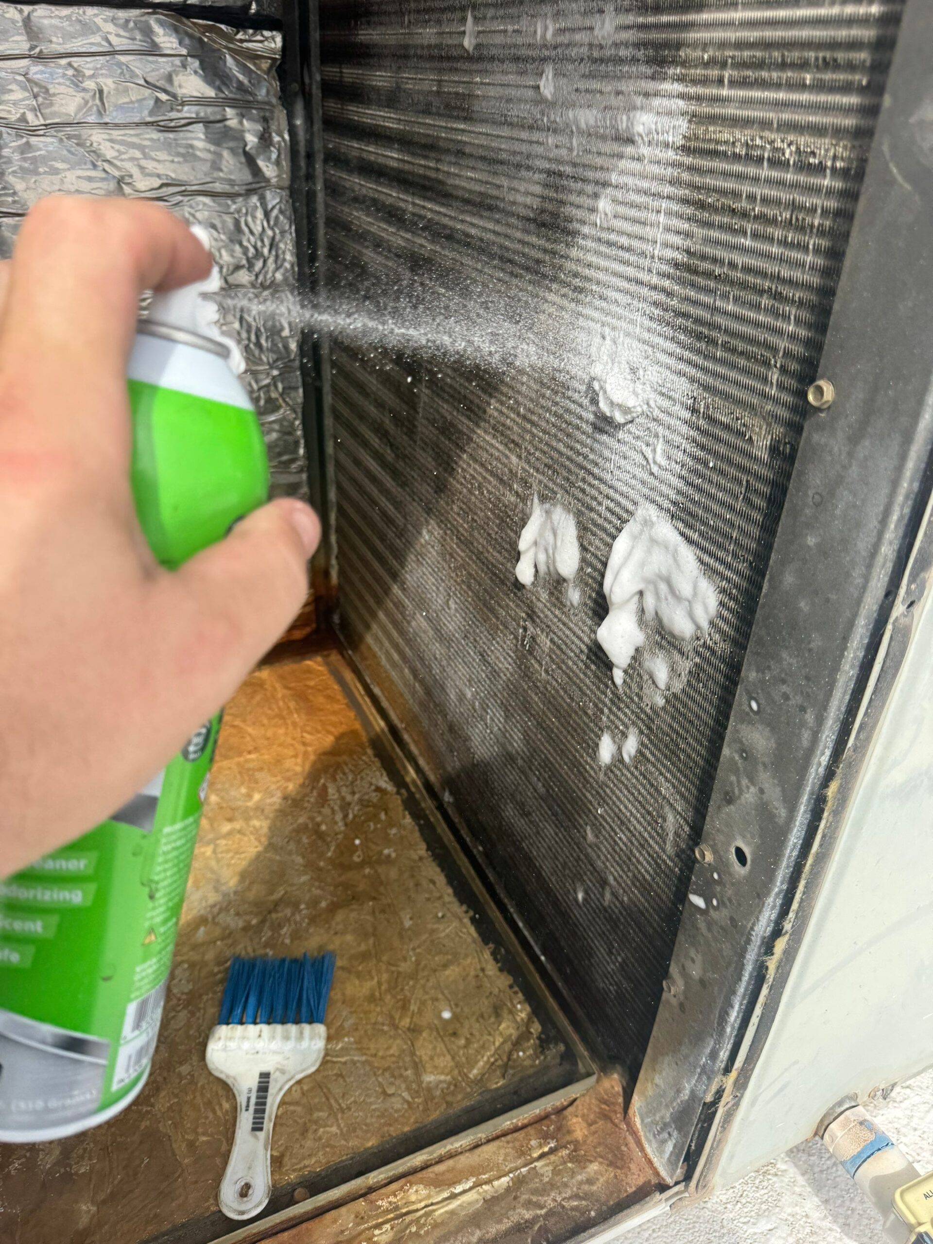 A technician cleaning an AC coil with foaming cleaner during a tune-up
