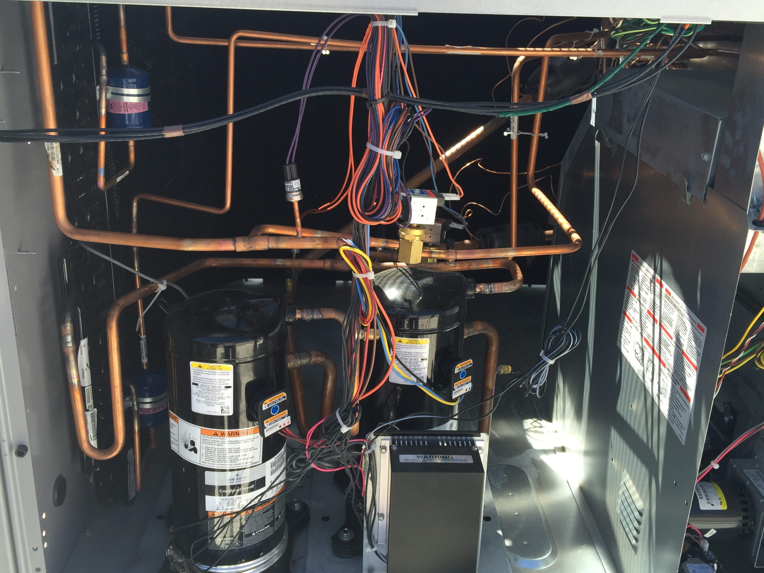 The inside of an HVAC unit showing the compressor and copper lines