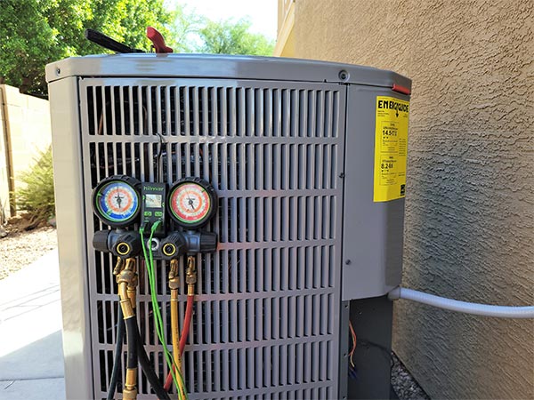 A condenser unit with manifold gauges connected during an AC repair