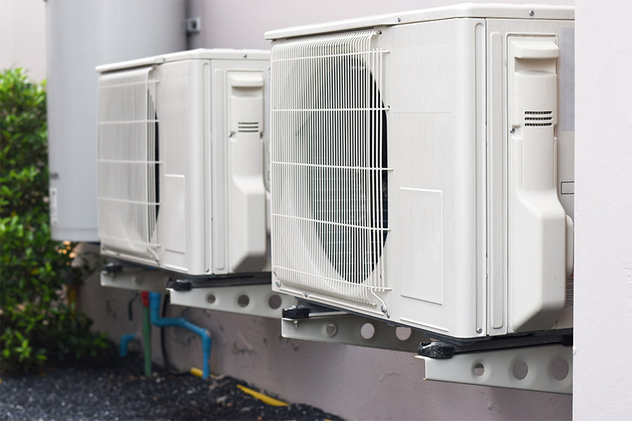 Two white ductless mini split outdoor units mounted on a wall