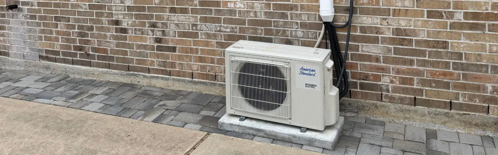 A mini split condenser unit installed on pavers against a brick wall